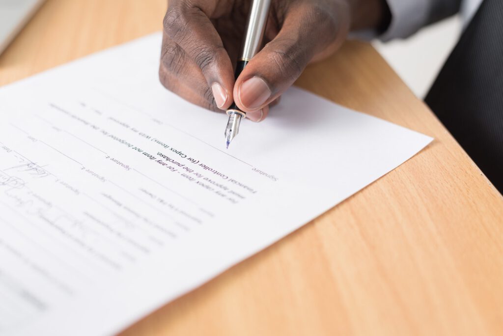 Nahaufnahme einer Hand die einen Füller hält um eine Unterschrift unter einen Vertrag zu setzen.